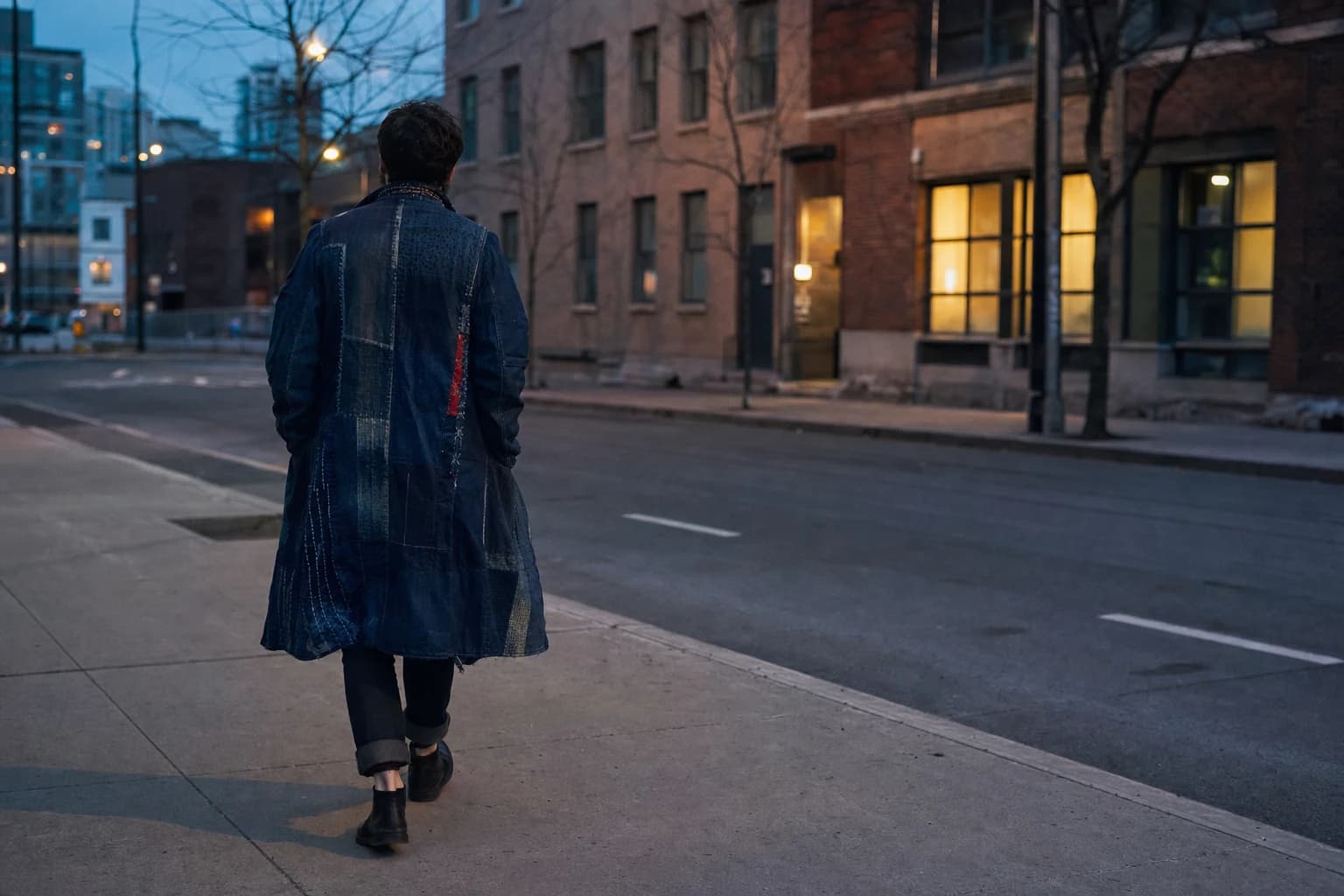 A person wears a visibly repaired indigo coat on a city street