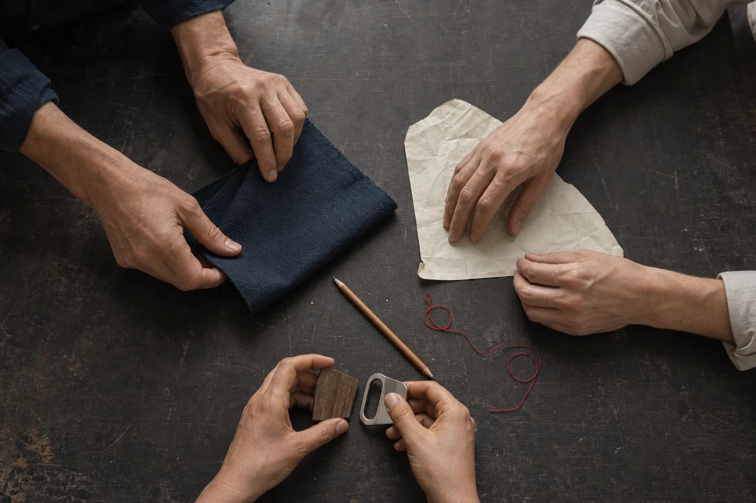 Three collaborators compare indigo cloth, paper, wood and metal around a worktable