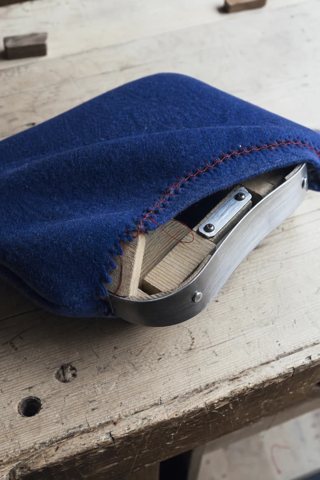 A cobalt wool object visibly repaired with scarlet thread over wood and brushed metal