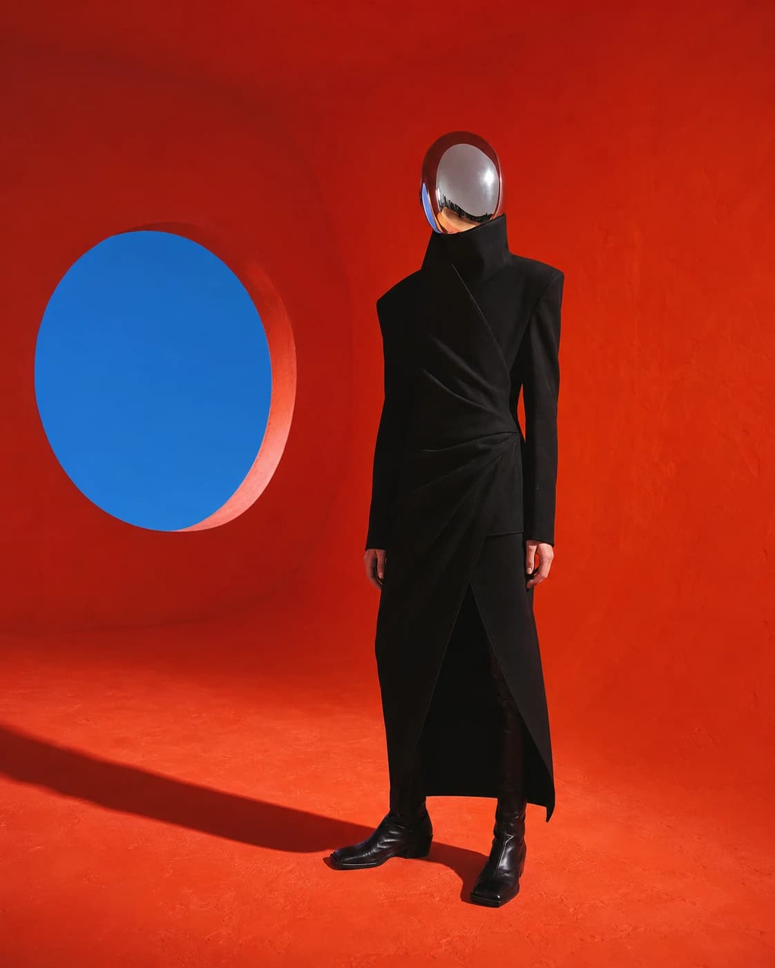 A figure in a black architectural coat and mirrored visor